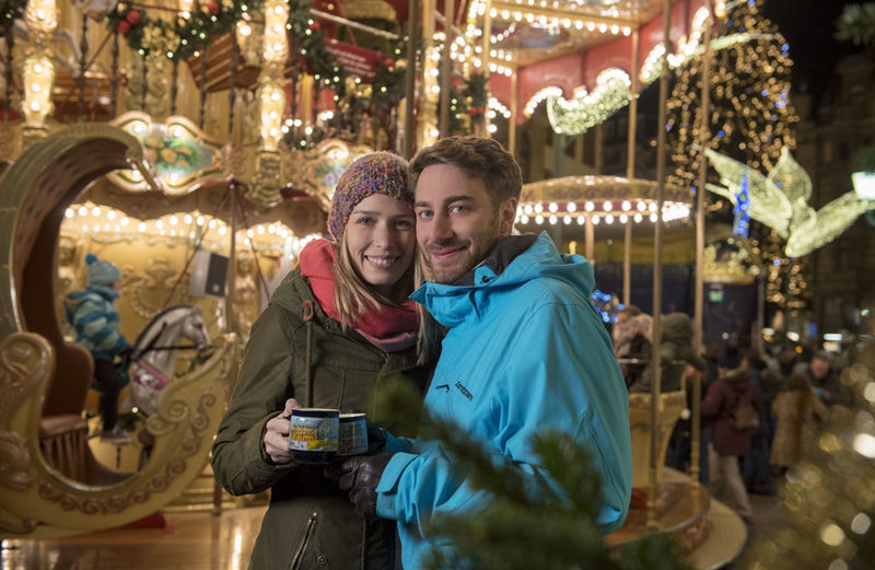 Weihnachtlichen Kurzrundgänge Sternschnuppenmarkt: Junges Paar am Karussell mit Glühwein.