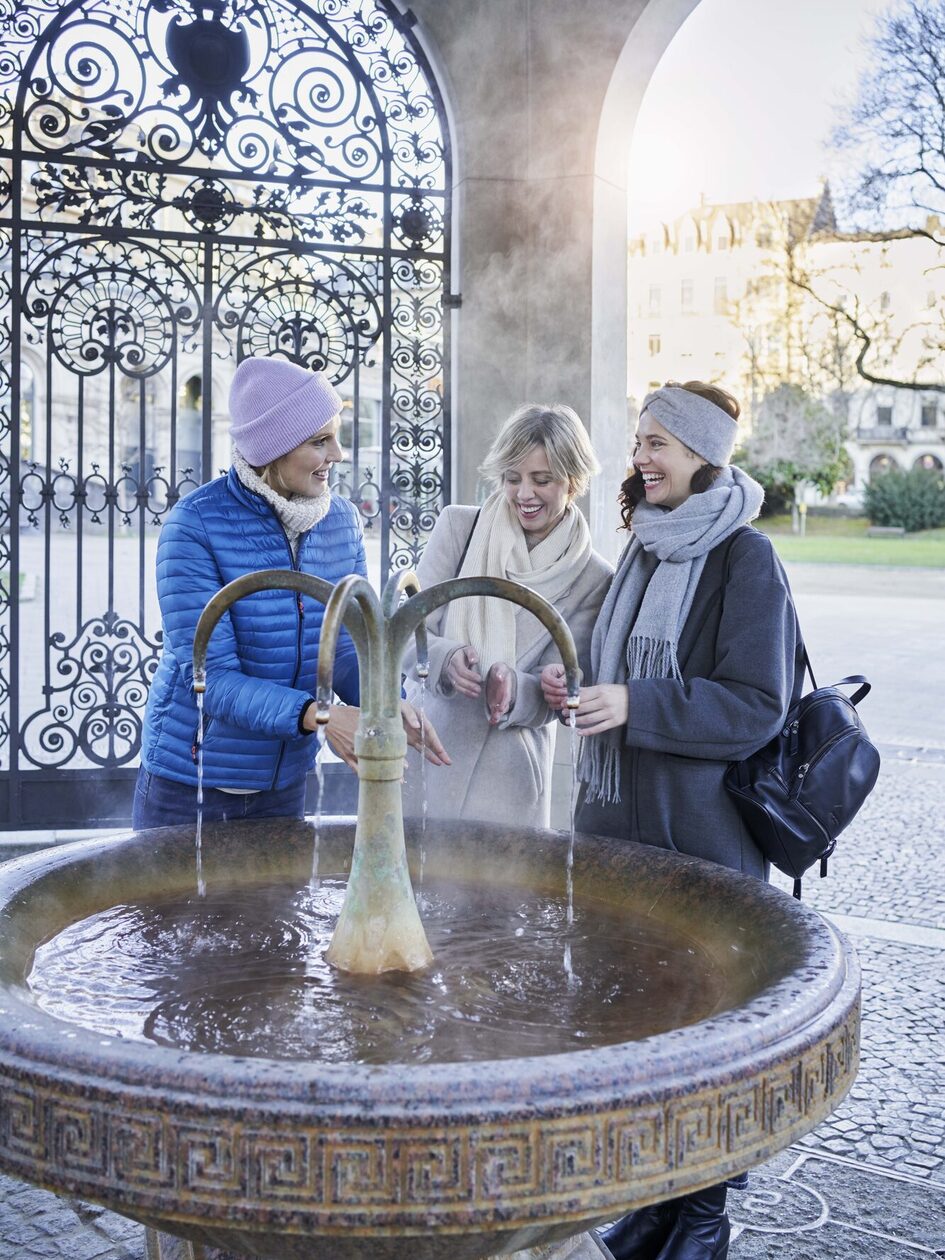 Drei Frauen trinken wasser am Kochbrunnen