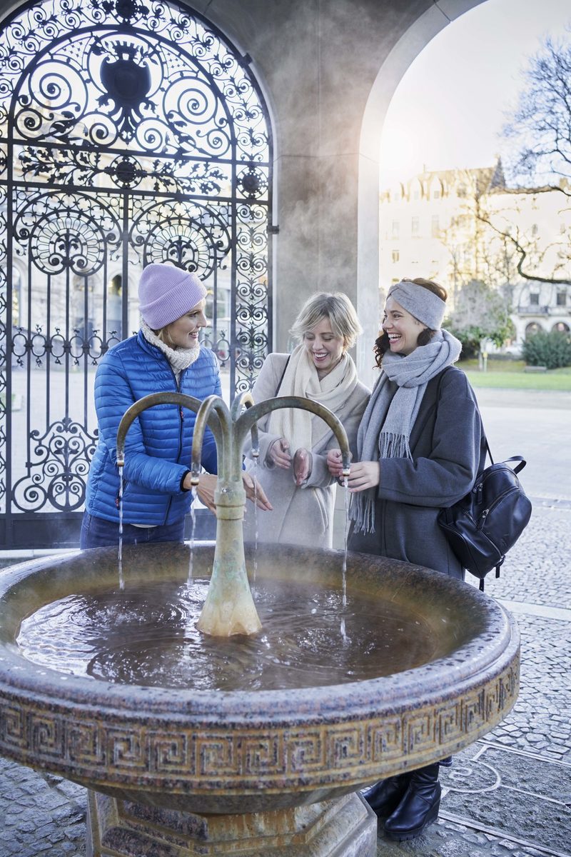 Drei Frauen trinken wasser am Kochbrunnen