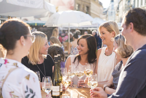 Menschen stehen in fröhlicher Runde an einem Tisch und genießen ihren Wein.