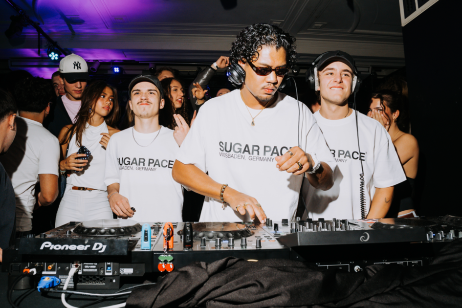 Mann am DJ Pult und tanzende Menschen im Hintegrund