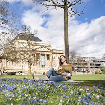 Frau sitzt lesend vor dem Hessischen Staatstheater