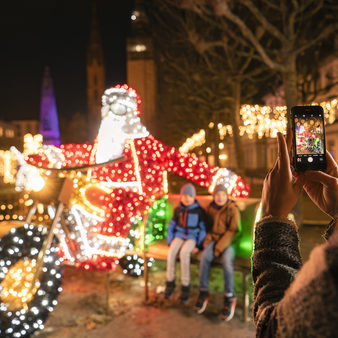 Kinder auf einer Bank neben einer Nikolausfigur auf einem Motorrad aus Lichtern