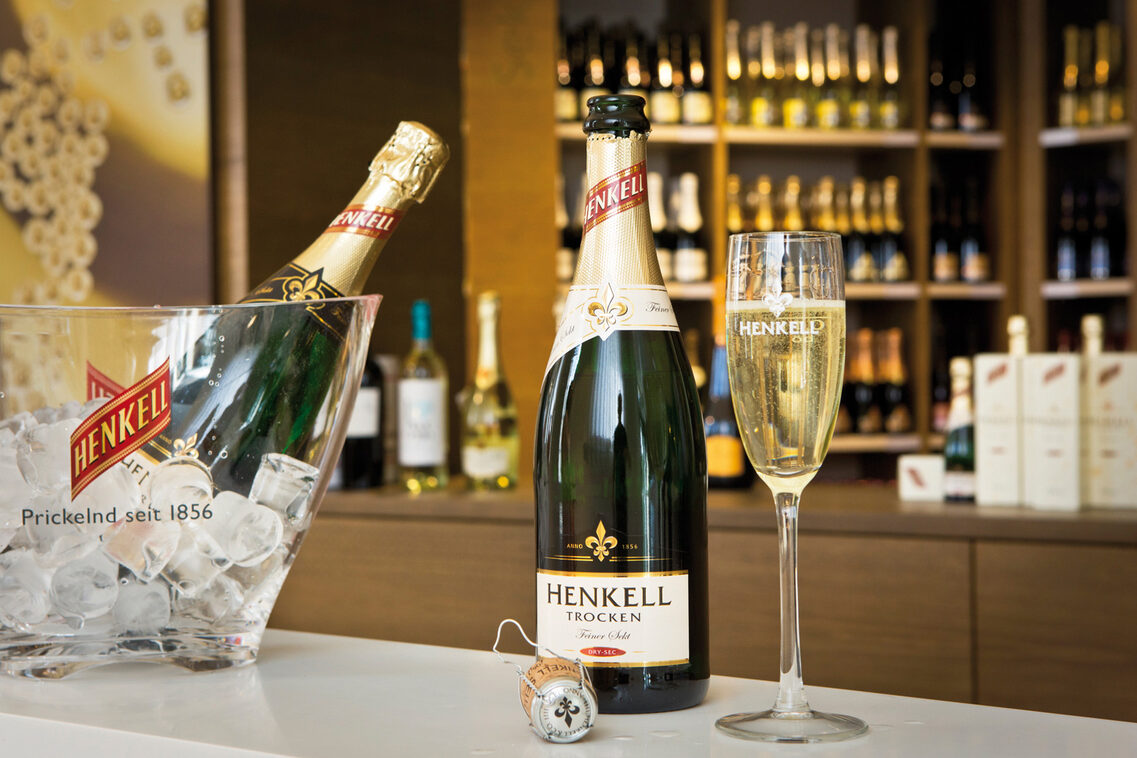 Henkell champagne bottle and glass in front of filled shelves