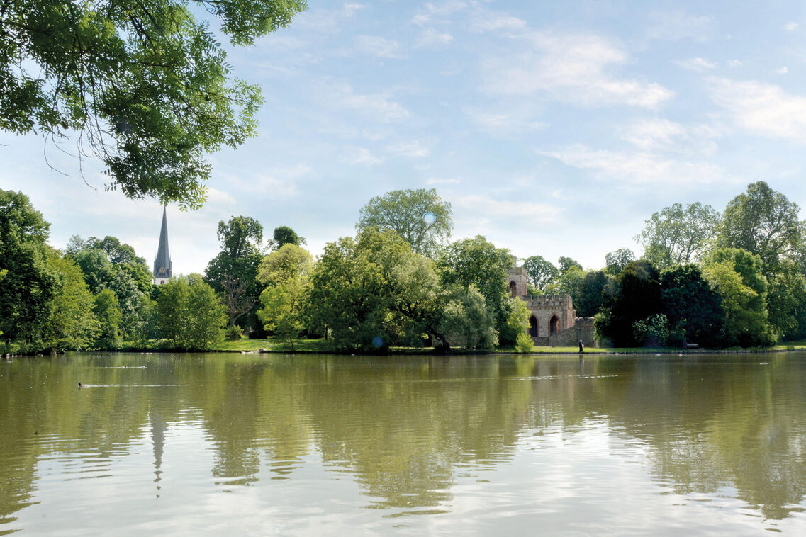 Pond in the castle park with small castle and visible church spire