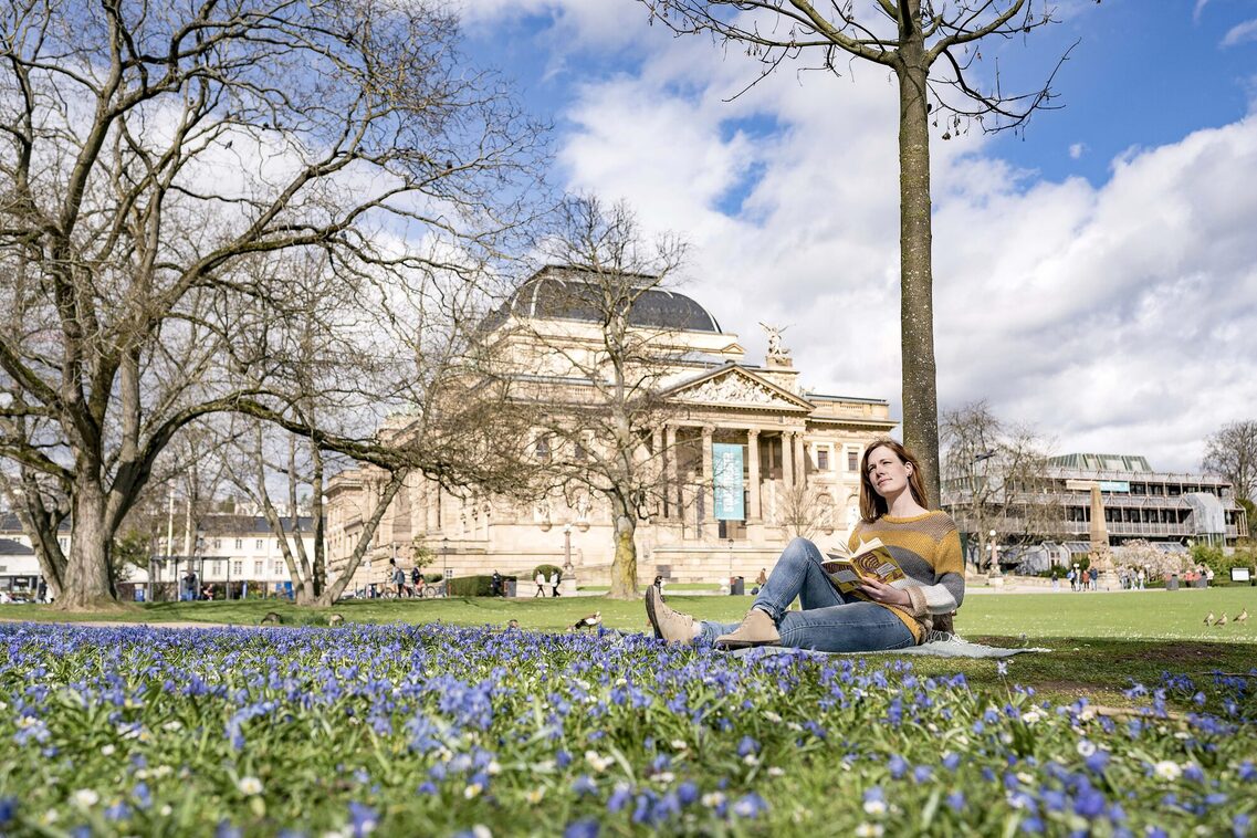 Frau sitzt lesend vor dem Hessischen Staatstheater