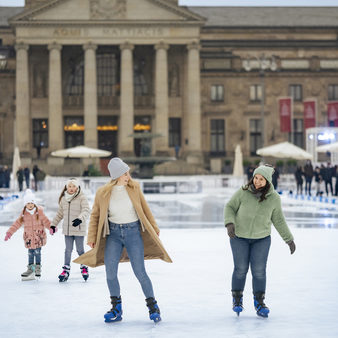 Zwei Frauen laufen Schlittschuh auf der Eisbahn vor dem Kurhaus.