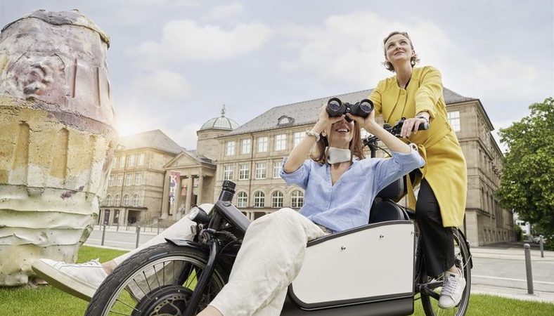 Zwei Frauen auf dem Fahrad vor dem Museum