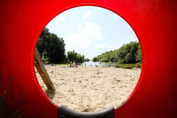 Sand, Wasser und Bäume durch ein Fenster mit rotem Rahmen.