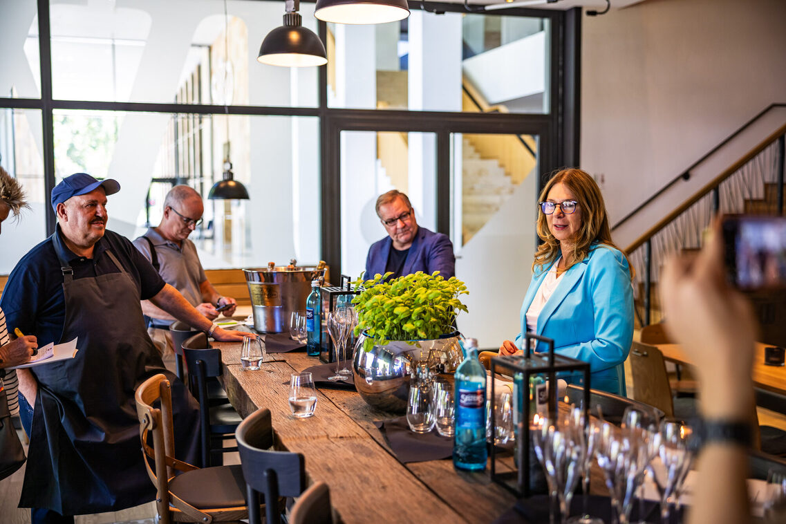 Drei Männer und eien Frau stehen am Tisch und unterhalten sich