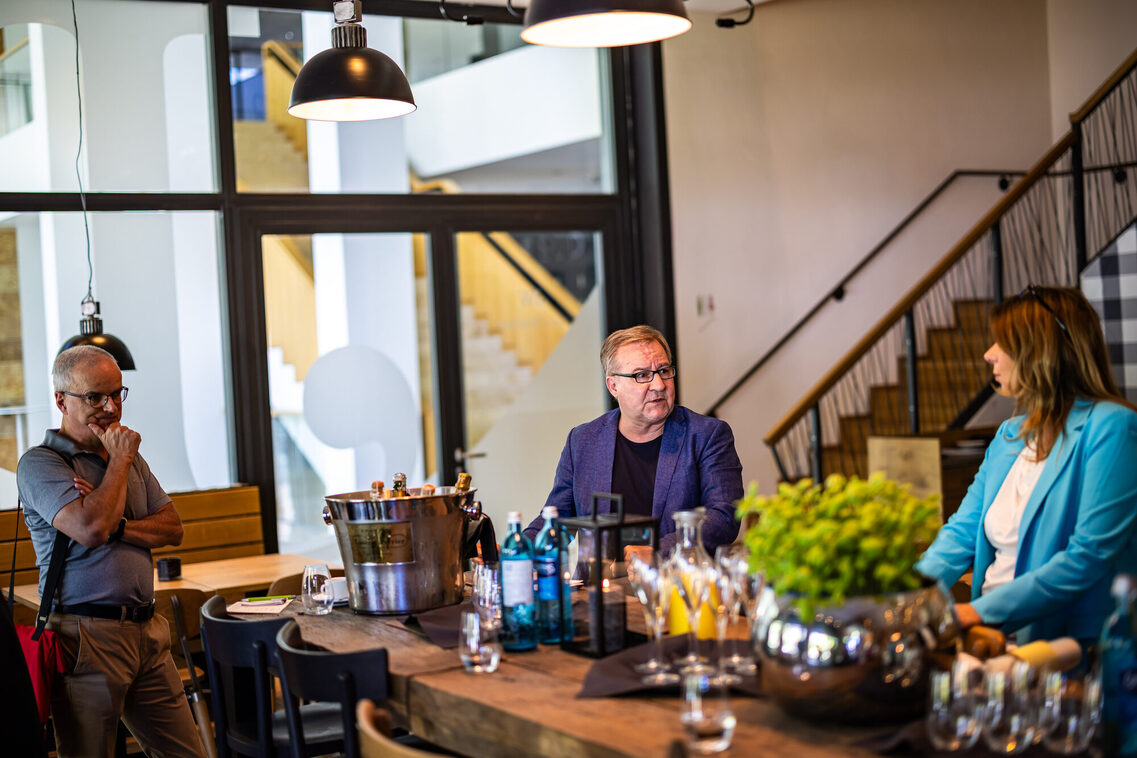 Zwei Männer und eine Frau stehen am Tisch und unterhalten sich